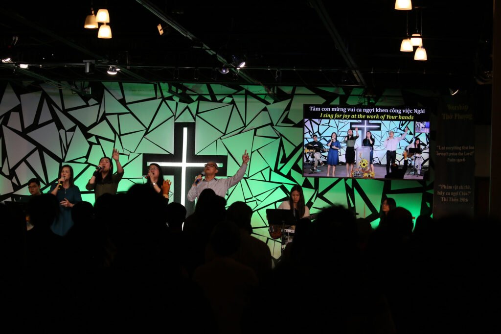 Worship team singing, with lyrics on screen in Vietnamese and English
